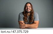 Smiling Man With Long Hair Embodies Confidence and Approachability in a Minimalist Setting. Стоковое AI-изображение, AI-художник Sergey Grishin / Фотобанк Лори