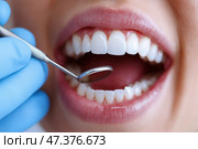 Dentist examines patients teeth with instrument during dental checkup. Стоматолог в синих перчатках внимательно осматривает рот пациента с помощью стоматологического зеркала. Обстановка - яркий, современный стоматологический кабинет, подчеркивающий важность здоровья полости рта. Стоковое AI-изображение, AI-художник Katsiaryna Repich / Фотобанк Лори