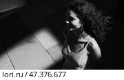 Woman walking in a sunlit corridor with shadows at noon. Женщина с вьющимися волосами улыбается, проходя по светлому коридору, наполненному контрастными тенями. Солнечный свет придает сцене глубину, пока она наслаждается моментом. Стоковое AI-изображение, AI-художник Katsiaryna Repich / Фотобанк Лори