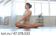 Positive young fit girl in sportswear doing yoga in modern mirrored studio, concentrating on performing revolved easy pose, basic seated posture with crossed legs and twist increasing flexibility. Стоковое видео, видеограф Яков Филимонов / Фотобанк Лори