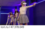 Four cheerful emotional young female friends in VR goggles standing in virtual reality room, manipulating objects or shooting at targets with gaming controllers in hands. Стоковое видео, видеограф Яков Филимонов / Фотобанк Лори