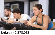European is exercising on an exercise bike in the gym. Young woman focused while keeping pace on stationary bike. Стоковое видео, видеограф Яков Филимонов / Фотобанк Лори