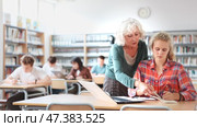 Mature female teacher working with schoolchildren in the library cheks the assignment from a European fifteen-old-year schoolgirl. Стоковое видео, видеограф Яков Филимонов / Фотобанк Лори