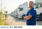 Experienced truck driver in blue polo shirt standing with arms crossed near modern trucks, professional transport service, freight company, logistics business, cargo delivery, road transportation. Стоковое AI-изображение, AI-художник Павел Муравьев / Фотобанк Лори
