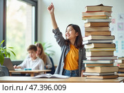 Счастливая девушка, поднимающая руку в классе, наполненном книгами. Стоковое AI-изображение, AI-художник Елена Болотина / Фотобанк Лори
