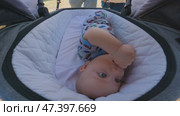 The baby is lying in stroller, dressed in a colorful jumpsuit with pictures of cars. The stroller is covered with white quilted fabric. The parents push stroller through park. A close-up of baby. Стоковое видео, видеограф Воловодов Владимир / Фотобанк Лори