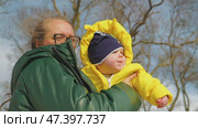 A woman in a green down jacket holds an infant in a bright yellow winter coat against a winter sky. Mother and son on a walk in the park. Close-up, view from below. Стоковое видео, видеограф Воловодов Владимир / Фотобанк Лори