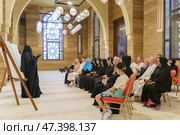 Manama, Bahrain - Jan 15 2024, An Arab woman dressed in a black burqa and niqab enthusiastically tells group of tourists about history of Islam inside of the Grand Mosque Al Fateh, Manama, Bahrain. Редакционное фото, фотограф Сергей Богомяко / Фотобанк Лори