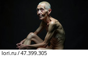 Elderly Person Seated in a Dark Environment With a Thoughtful Expression and Unique Posture, Showcasing the Beauty of Aging and Life Experience. Dystrophy, anorexia. Стоковое AI-изображение, AI-художник Sergey Grishin / Фотобанк Лори