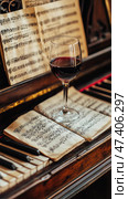 Elegant Wine Glass Rests on Sheet Music Atop a Vintage Piano During a Cozy Evening at Home. Стоковое AI-изображение, AI-художник Юлия Гапеенко / Фотобанк Лори