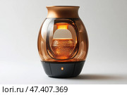 A modern designer device with an elegant shape, made in a glossy amber-transparent case with a black base. Inside is a glowing element reminiscent of a honeycomb or candle structure, emitting a soft, warm light. The upper part is open - perhaps it is an aroma diffuser, a smart lamp, an air purifier or a decorative humidifier. The style is minimalist and futuristic, ideal for interiors in the spirit of high-tech, loft or modern. Стоковое AI-изображение, AI-художник Анна Кривицкая / Фотобанк Лори