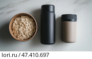Fitness essentials for a healthy lifestyle including a water bottle and bowl. Три предмета первой необходимости для фитнеса, выставленные на столе: чаша с овсянкой, бутылка с водой и два контейнера для питания, освещенные естественным солнечным светом в минималистской обстановке. Стоковое AI-изображение, AI-художник Katsiaryna Repich / Фотобанк Лори