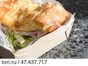 Сэндвич с вкуснейшим свежим хлебом с хрустящей корочкой и ветчиной в оберточной бумаге и картонном подносе, купленный на фуд-корте. Стоковое фото, фотограф Татьяна Васильева / Фотобанк Лори