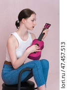 Serious young female musician playing ukulele, sitting on bar stool and looking away. Стоковое фото, фотограф А. А. Пирагис / Фотобанк Лори