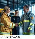 A warm moment of meeting and cooperation between emergency services. A woman in a yellow firefighter's uniform shakes hands with a man in a medical gown with reflective elements. He is a doctor or paramedic. In the background, another woman in a dark blue uniform smiles, probably an emergency services worker or administrator. They are all in a modern building or hangar, possibly an emergency services base. The atmosphere is positive and respectful, emphasizing the importance of interdepartmental cooperation. Стоковое AI-изображение, AI-художник Анна Кривицкая / Фотобанк Лори