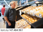 Man takes muffins on shelf of bakery section. Стоковое фото, фотограф Татьяна Яцевич / Фотобанк Лори