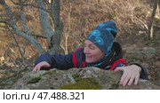 A young female hiker attempts to climb a moss-covered rock surrounded by a serene natural landscape of trees and undergrowth. Gives up and cannot climb. Стоковое видео, видеограф Воловодов Владимир / Фотобанк Лори