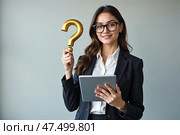 Уверенная женщина в черном костюме держит золотой вопросительный знак и планшет на сером фоне, концепция запроса, место для текста. Стоковое AI-изображение, AI-художник Елена Болотина / Фотобанк Лори