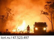 A solitary firefighter combats an overwhelming forest blaze. Enveloped by fire, the scene captures the peril and heroism of battling towering flames amid an environmental disaster. Стоковое AI-изображение, AI-художник Nart / Фотобанк Лори