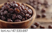 Dark raisins displayed in a wooden bowl on a rustic table setting. Темный изюм в деревянной миске на столе в деревенском стиле. Стоковое AI-изображение, AI-художник Katsiaryna Repich / Фотобанк Лори