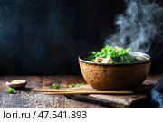 A steaming bowl of miso soup sits on a dark backdrop, exuding warmth and comfort. The savory Japanese broth features rich umami flavors, highlighted by its moody and atmospheric presentation. Стоковое AI-изображение, AI-художник Nart / Фотобанк Лори