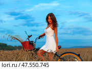 Brunette woman in white dress with bicycle in wheat field at sunset. Стоковое фото, фотограф Nobilior / Фотобанк Лори