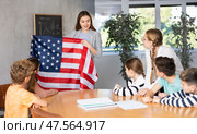 Positive female teacher discussing with preteens students American flag in auditory of middle school. Стоковое фото, фотограф Яков Филимонов / Фотобанк Лори