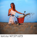 Brunette woman in white dress with bicycle in wheat field at sunset. Стоковое фото, фотограф Nobilior / Фотобанк Лори