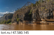 A calm red-brown African river with steep rocky shores. There is green vegetation on the eroded limestone slopes. Blue sky, clouds. Madagascar. Manambolo river (2023 год). Стоковое фото, фотограф Вера Ивановна Кубарева / Фотобанк Лори