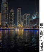 UAE, Dubai, 10 December 2024: Mosque of Muhammad Ibn Ahmad Al-Mullah against the backdrop of skyscrapers at night in Dubai Marina, yachts sailing by, reflection of night lighting on the water. Редакционное фото, фотограф Vladimir Drozdin / Фотобанк Лори
