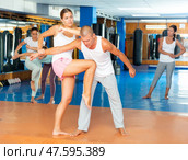 Girl performing elbow and knee strikes with arm hold to male sparring partner in gym. Стоковое фото, фотограф Яков Филимонов / Фотобанк Лори