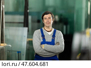 Man glazer employee in blue overall works in glass processing shop. Стоковое фото, фотограф Яков Филимонов / Фотобанк Лори