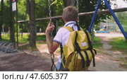The schoolboy sways on a swing with a backpack at the school. Стоковое видео, видеограф Igor Skripachev / Фотобанк Лори