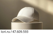 White baseball cap mockup displayed on a sleek stand against a neutral background. Белая бейсболка на изящной подставке на нейтральном фоне. Стоковое AI-изображение, AI-художник Katsiaryna Repich / Фотобанк Лори