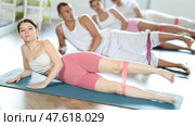 Flexible athletic young woman lying on side practicing fitness during group exercise with elastic band stretching legs muscles in sports club. Стоковое видео, видеограф Яков Филимонов / Фотобанк Лори
