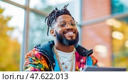 Portrait of Smiling Man with Dreads, Glasses, & Vibrant Jacket, Radiating Happiness, Positive Vibes. Стоковое AI-изображение, AI-художник Данила Большаков / Фотобанк Лори