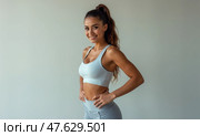 Confident Woman Posing in Athletic Wear, Smiling and Looking at the Camera Against a Plain Background; Can Be Used by Fitness Brands, Gyms, or Wellness Studios. Стоковое AI-изображение, AI-художник Sergey Grishin / Фотобанк Лори