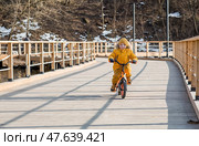 A cute boy in bright yellow clothes rides a bike. A happy child plays outside in early spring. Happy childhood. Стоковое фото, фотограф Photojuli / Фотобанк Лори