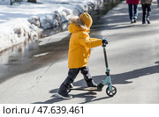 A little boy in bright yellow clothes rides a scooter. A happy child walks outside in early spring. Happy childhood. Стоковое фото, фотограф Photojuli / Фотобанк Лори