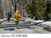 A little boy in bright yellow clothes and his dad ride scooters. A happy child and father are walking outside in early spring. Happy childhood and family. Стоковое фото, фотограф Photojuli / Фотобанк Лори