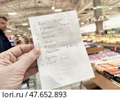 Kirov, Russia - March 14, 2025: Grocery list in hand while shopping at a supermarket during daylight, capturing everyday life and errands. Редакционное фото, фотограф Кривошеина Елена Леонидовна / Фотобанк Лори