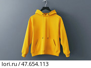 Blank yellow hoodie sweatshirt long sleeve hanging on simple hook against a gray wall. Hoody with hood. Design, print mockup. Template sport clothes. Front view. Gender neutral. Brand, logo. Стоковое AI-изображение, AI-художник Марина Демидюк / Фотобанк Лори