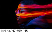 A striking portrait of a young woman, her face partially obscured by vibrant streaks of light, wearing glasses and a hooded jacket, against a black background. Стоковое AI-изображение, AI-художник Данила Большаков / Фотобанк Лори