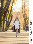 Happy young woman walks in the autumn park. An attractive woman with light brown hair and a gray coat is walking down the alley. Beautiful autumn mood. Fall season. Стоковое фото, фотограф Андрей Степанов / Фотобанк Лори