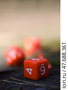 Крупный план красного шестигранного игрального кубика (D6), показывающего числа 4, 5, 6, лежащего на темной деревянной поверхности (пень) с размытым фоном. Игра, удача. Стоковое фото, фотограф Евгений Ковальский / Фотобанк Лори