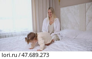 Attractive young woman and little cute girl are spending time together in bedroom at home. Mother with baby daughter lying on bed, hugging and having fun. Happy family concept. Mother's day footage. Стоковое видео, видеограф Ирина Михайличенко / Фотобанк Лори