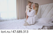 Attractive young woman and little cute girl are spending time together in bedroom at home. Mother with baby daughter jumping on bed, hugging and having fun. Happy family concept. Mother's day. Стоковое видео, видеограф Ирина Михайличенко / Фотобанк Лори