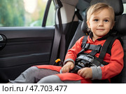 The child is sitting in the car, securely fastened with seat belts in the car seat. Стоковое AI-изображение, AI-художник Ирина Старикова / Фотобанк Лори
