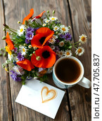 A beautiful bouquet of wild flowers with poppies and cammomille on an old wooden table. Nearby is a cup of hot coffee and a sheet of paper with the heart and copy space for text. Стоковое AI-изображение, AI-художник Iva Noel / Фотобанк Лори