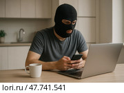 Киберпреступник. Человек в маске использует ноутбук и смартфон за столом в помещении для совершения киберпреступлений. Стоковое AI-изображение, AI-художник Башкирова Анна / Фотобанк Лори